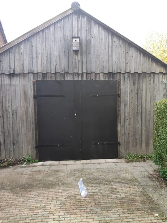 Dubbele zwarte garagedeur met hengsels in een houten gevel